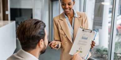 Businesswoman handing over a clipboard to a man in an office.