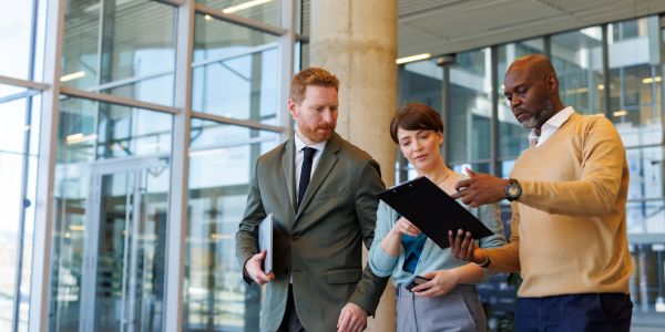 Three professionals discussing documents in a modern office building.