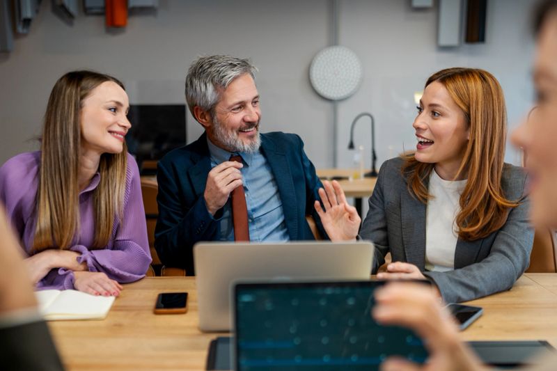 Group of diverse business professionals discussing ideas and smiling during a work meeting in a modern office environment