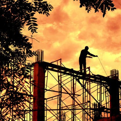 Silhouette of a worker on scaffolding against an orange sunset sky.