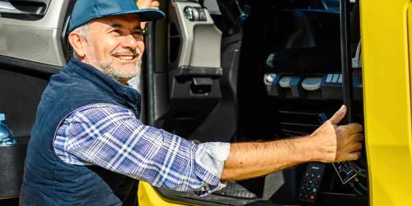 Smiling truck driver giving a thumbs up while sitting in his yellow truck.