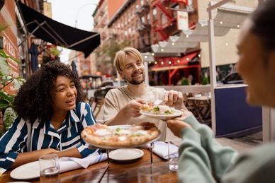 Friends sharing pizza at an outdoor restaurant.