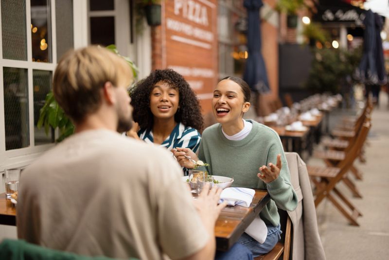 Group of diverse young adult friends enjoying a meal and conversation at an outdoor restaurant during the day