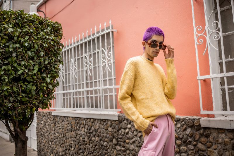 Non-binary person wearing a yellow sweater and pink pants, standing outdoors. Expressing self-identity and fashion