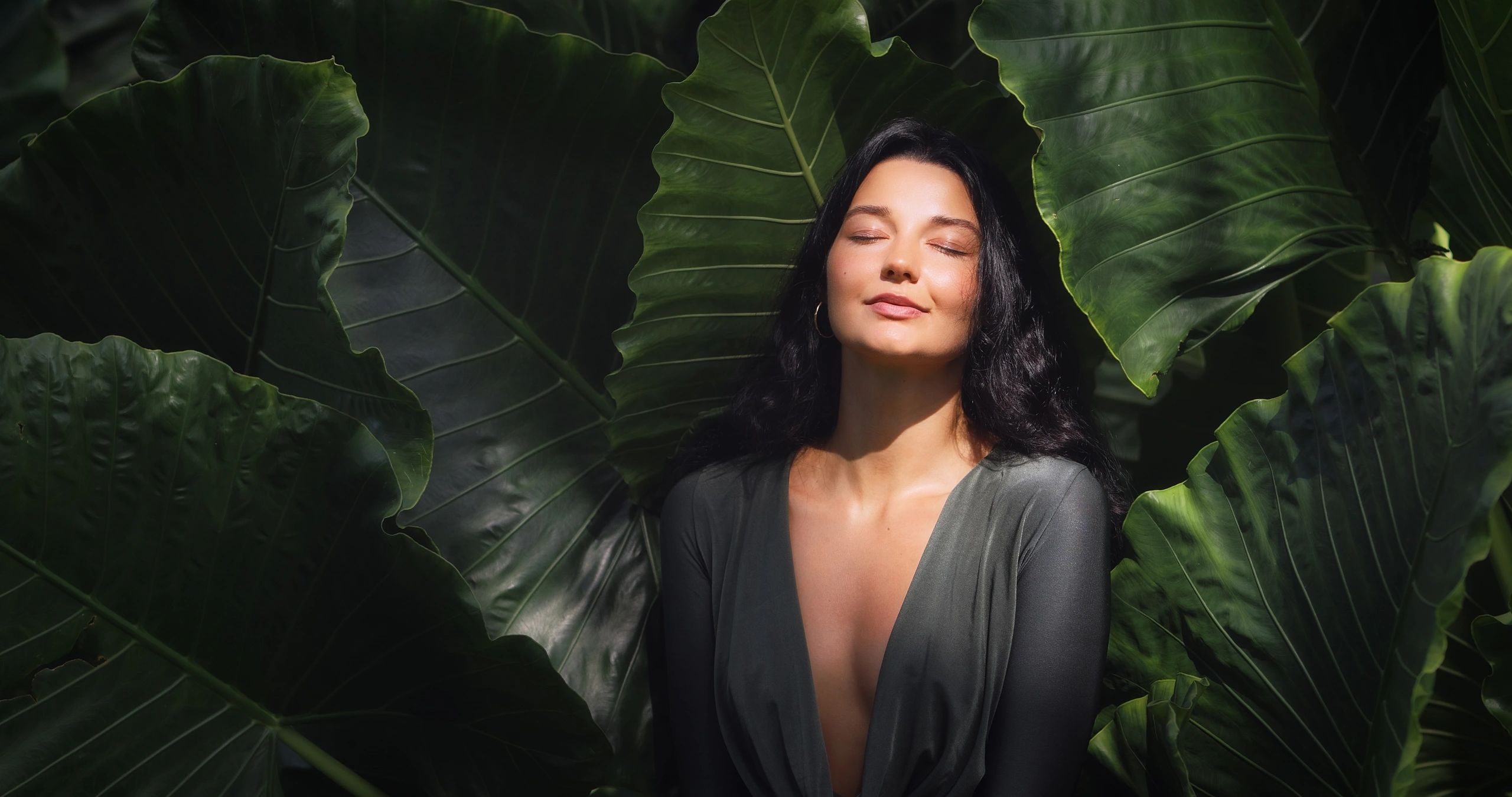 Woman peacefully surrounded by large green leaves.