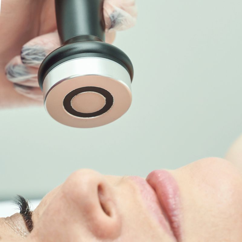 Caucasian female receiving facial treatment with ultrasound device in spa setting.