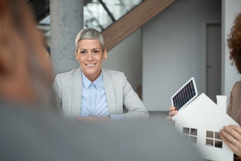 Professionals meeting to discuss sustainable living and green energy solutions, showcasing a house model with a solar panel, emphasizing environmental responsibility and future home investments