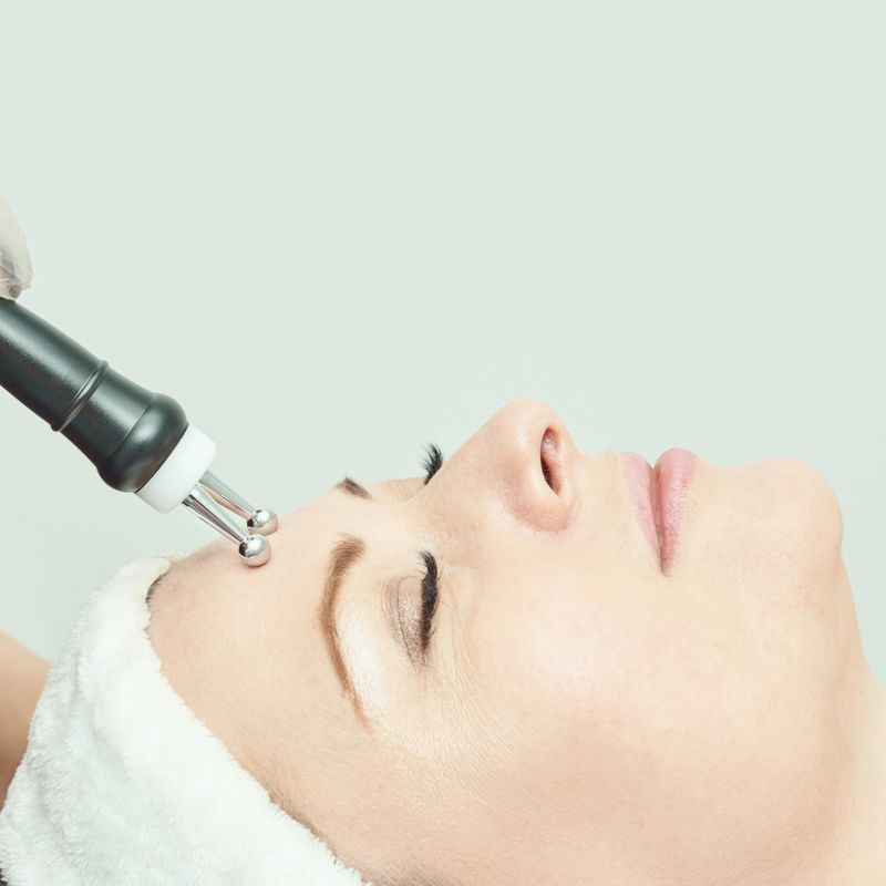 Caucasian female receiving facial microcurrent treatment in spa setting for skin rejuvenation.