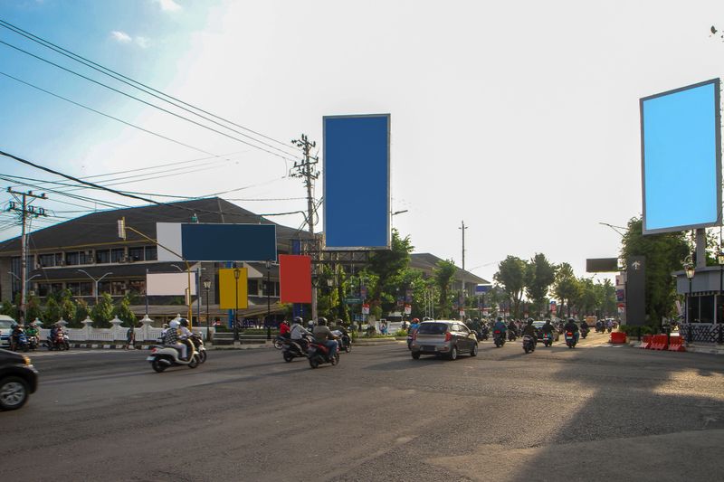Busy city intersection with motorcycles, cars, and multiple blank billboards for advertising mockups in Yogyakarta, Indonesia. Urban traffic scene with copy space for outdoor advertising concepts.