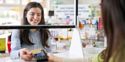 A smiling customer pays with a card at a pharmacy counter.
