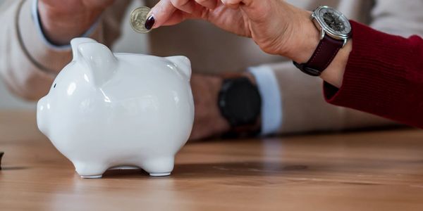 Person putting coin into white piggy bank.