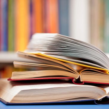 Stack of open books on a table with a blurred bookshelf background.