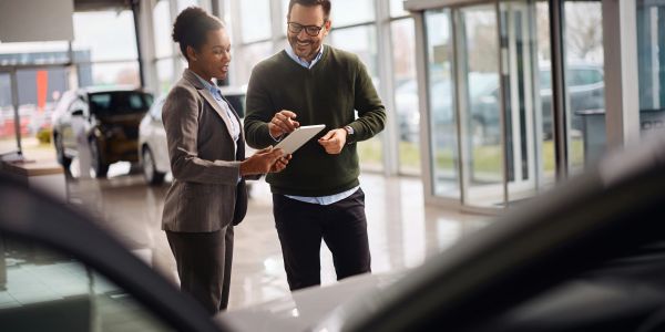 Car salesperson showing tablet to customer in dealership.