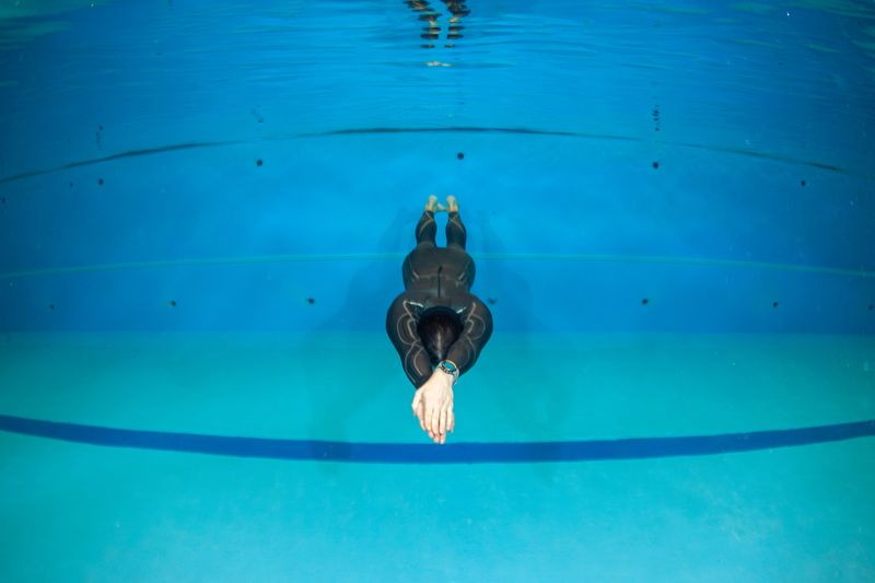 A swimmer in a black suit dives into the clear water of a swimming pool. This scene shows the swimmer preparing for a training session focused on improving their technique and form.
