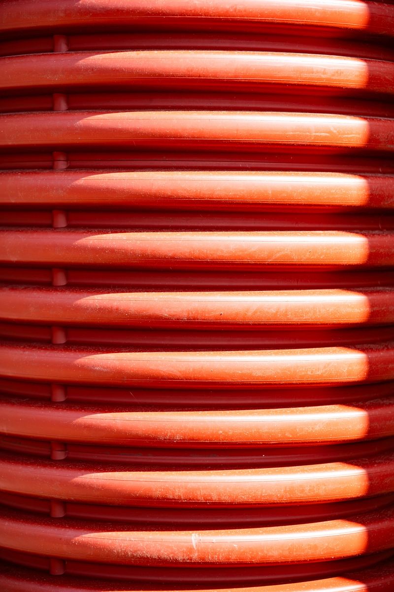 Red corrugated plastic pipe surface showing industrial texture, abstract pattern, and strong light