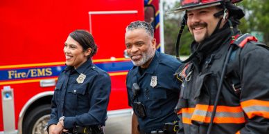 Three smiling first responders near a fire truck.