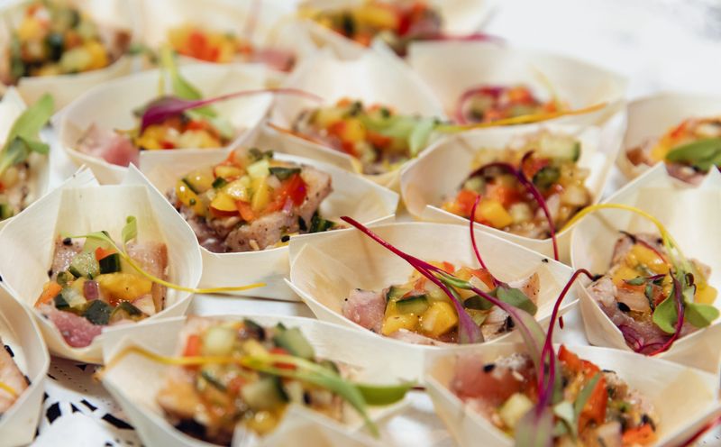 Gourmet tuna tartare appetizers topped with mango salsa and microgreens, presented in small bamboo cups for elegant catering, parties, weddings, and upscale buffet or cocktail receptions.