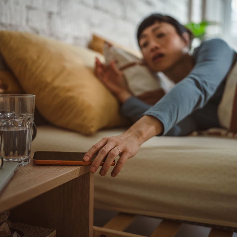 Woman waking up in bed, reaching for smart phone on nightstand to check messages or turn off alarm, cozy bedroom morning routine with casual, sleepy vibe