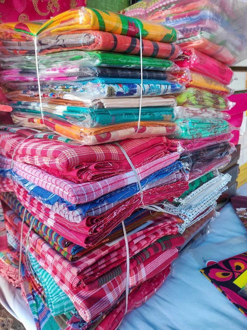 A stack of colourful, folded cotton and handloom fabric towels is displayed at a traditional textile market in India. Vibrant, handmade, patterned cloth bundles are neatly arranged for retail sale.