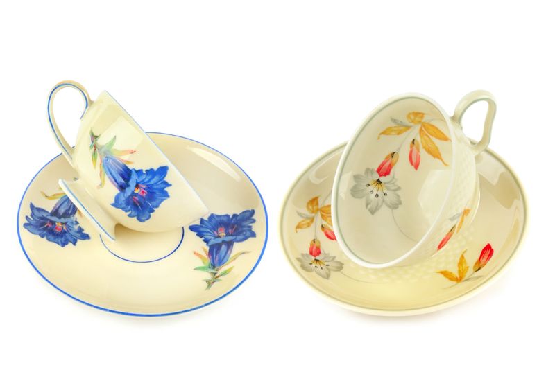 A pair of elegant vintage porcelain teacups and saucers featuring vibrant hand-painted floral motifs. This clean studio shot on white is perfect for lifestyle, home decor, or traditional tea content.