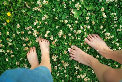 Two pairs of bare feet on clover grass with small white flowers.