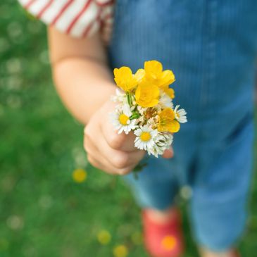 Child holding a small bouquet of yellow and white flowers.