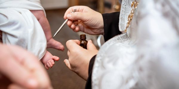 A priest anointing a baby's foot with oil during a religious ceremony.