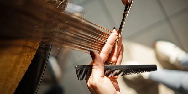 Close-up of a hairdresser trimming brown hair with scissors and a comb.