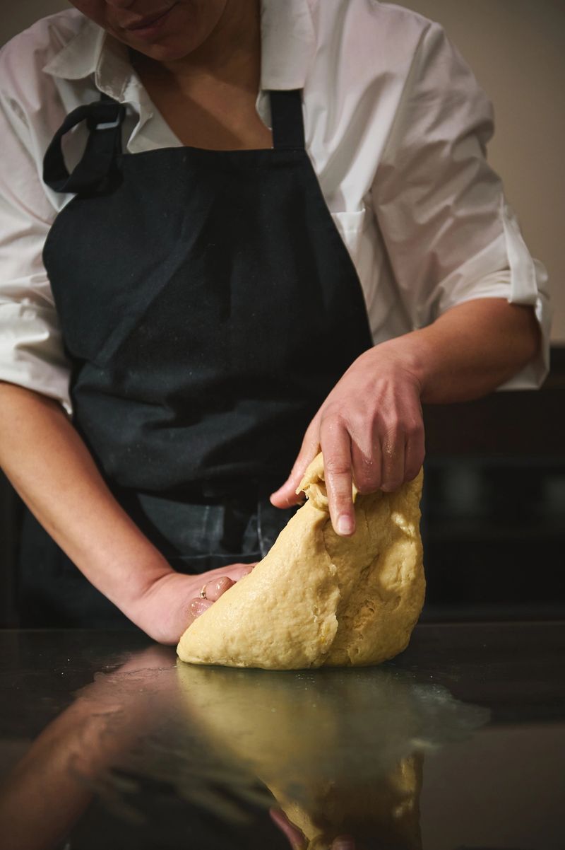 Female pastry chef in an apron kneads rich dough on a counter to prepare a handmade panettone, capturing hands-on baking technique and the warmth of home pastry making.