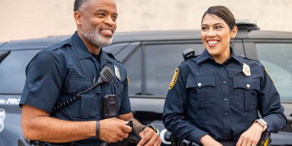 Two police officers smiling and standing by a patrol car.