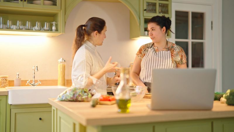 Happy women using laptop for online cooking class podcast, preparing together healthy vegetables in home kitchen. Dieting, detox, mindful eating & life balance