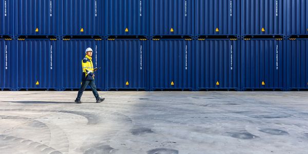 Worker walking in front of stacked blue shipping containers.
