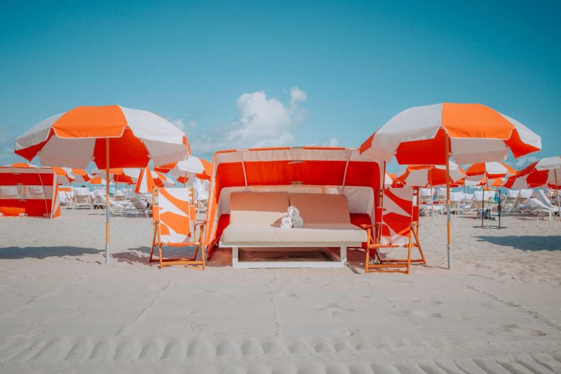 Orange and white umbrellas and a cabana stand in the morning sun ready for beachgoers