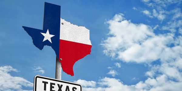Texas-shaped sign with state flag colors under a blue sky.