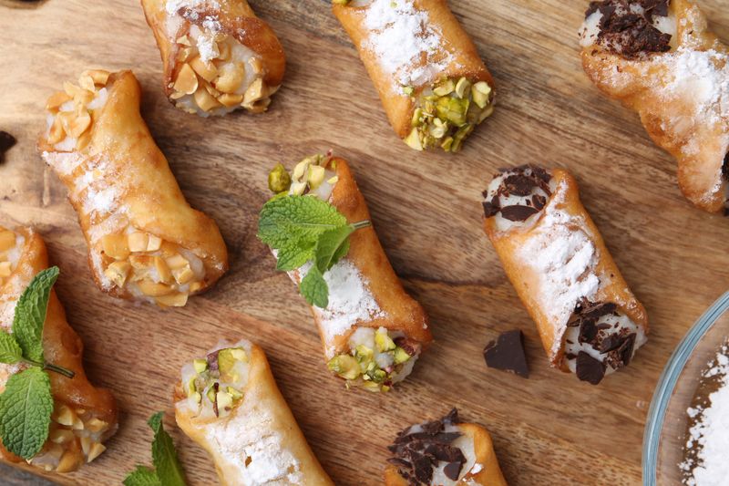 Delicious cannoli with cheese, nuts, chocolate, mint and powdered sugar on table, top view