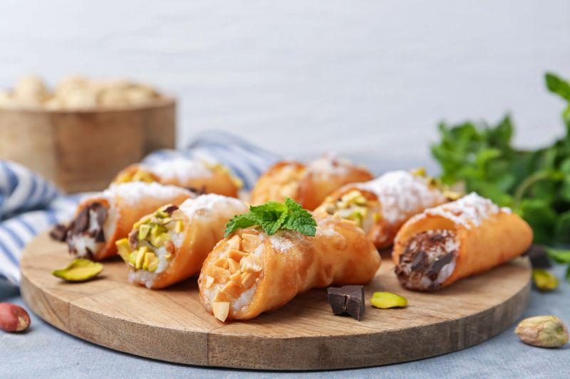 Delicious cannoli with cheese, nuts, powdered sugar, chocolate and mint on grey table, closeup