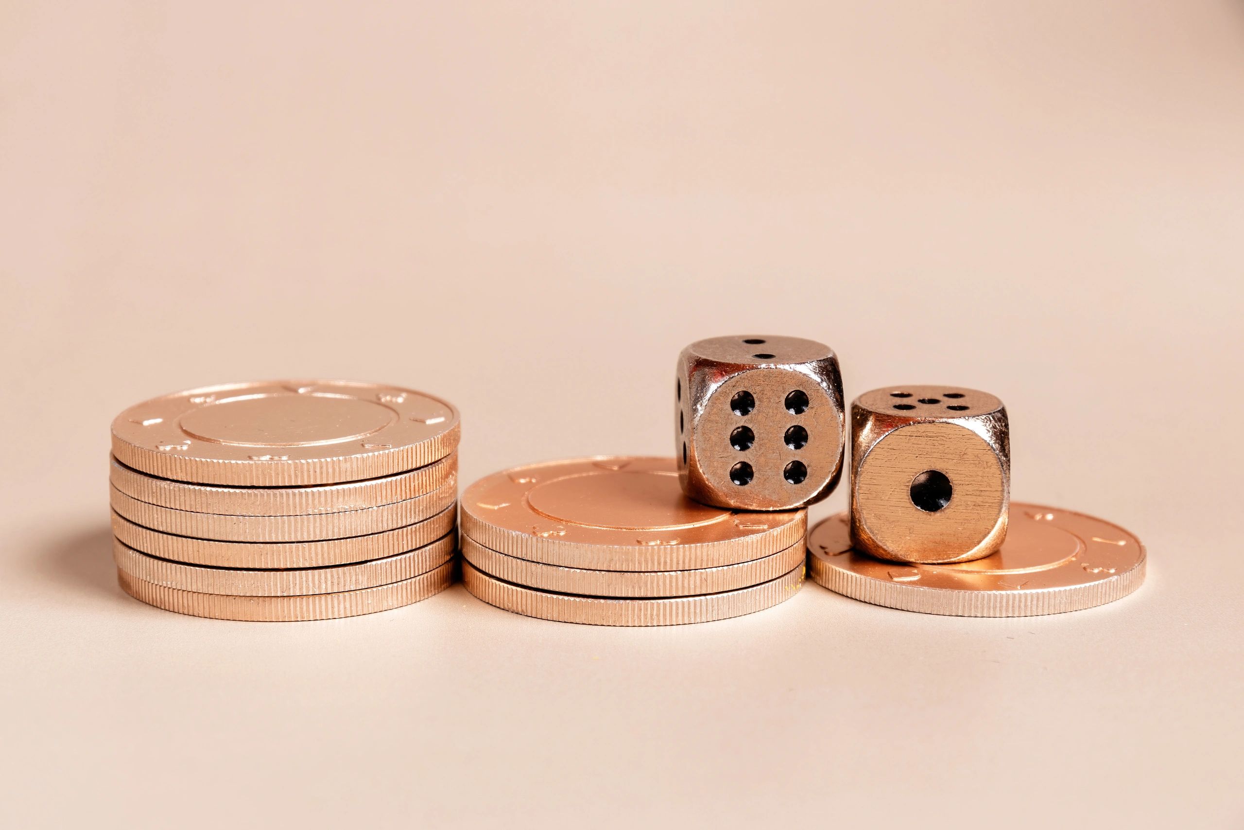 Metallic poker chips and dice on a beige surface.