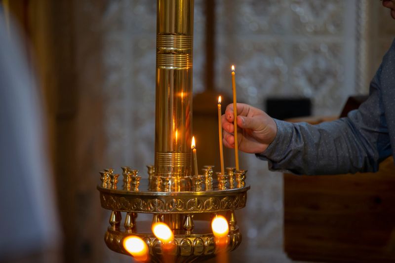 In a peaceful temple, a person lights candles on a decorative stand during a spiritual ceremony. The warm glow of the flames enhances the tranquil atmosphere, inviting reflection.