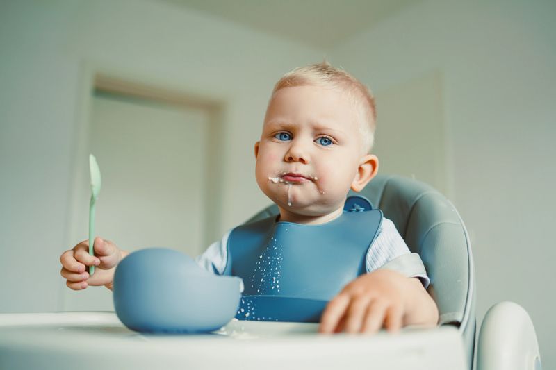 A twoyearold in a high chair explores colorful foods with a small spoon, demonstrating essential curiosity that aids their development during growthpromoting mealtimes