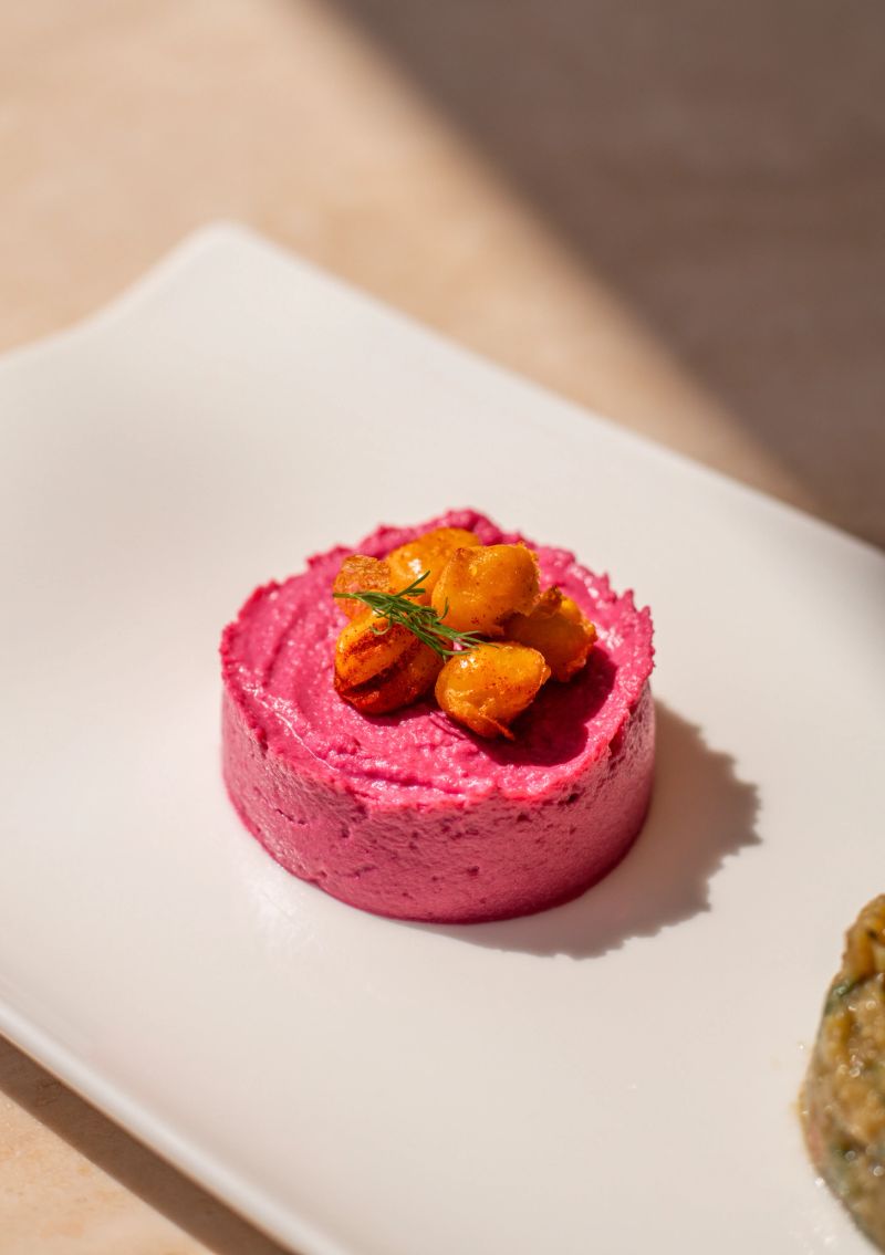 Meze beetroot hummus dip served on bright sunny table with crispy chick peas and olive in middle eastern gourmet restaurant
