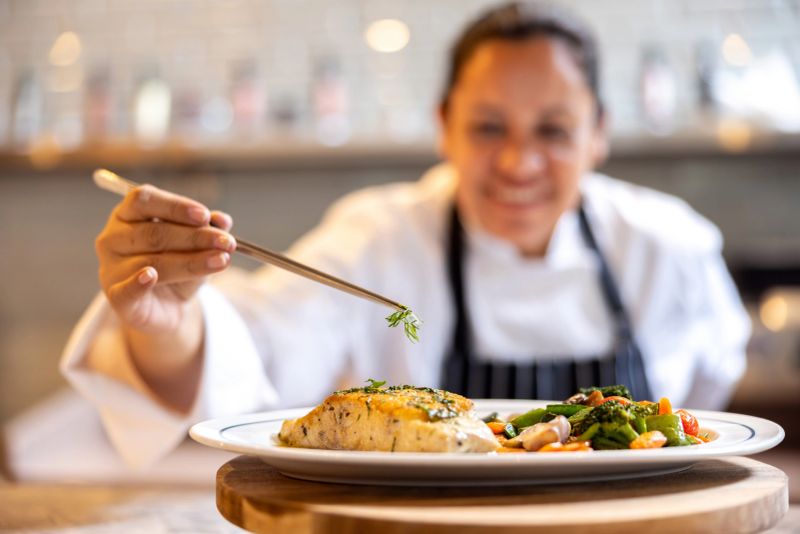 Happy Latin American chef decorating a plate while working at a gourmet restaurant