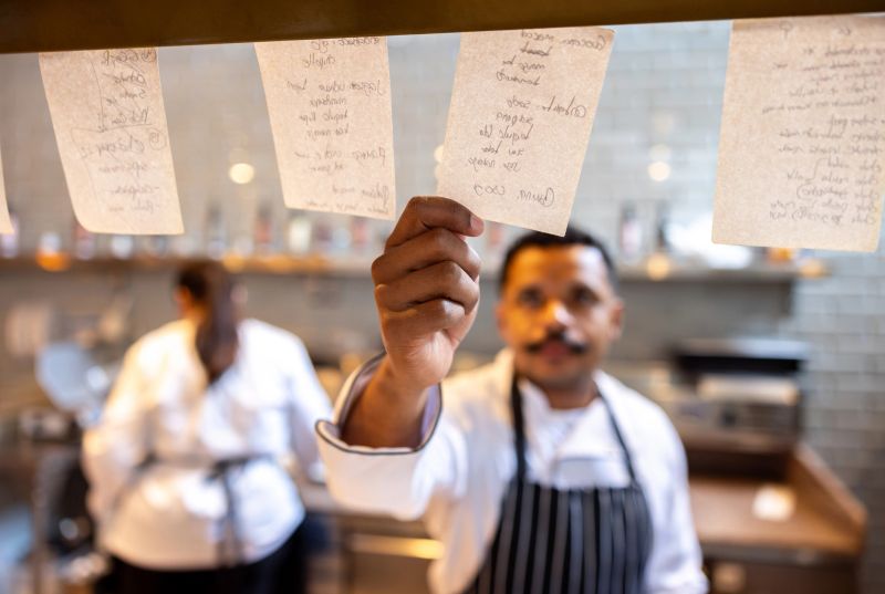 Latin American cook working at a restaurant and grabbing an order ticket in the kitchen