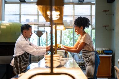 Chef handing a dish to a waitress in a restaurant kitchen.