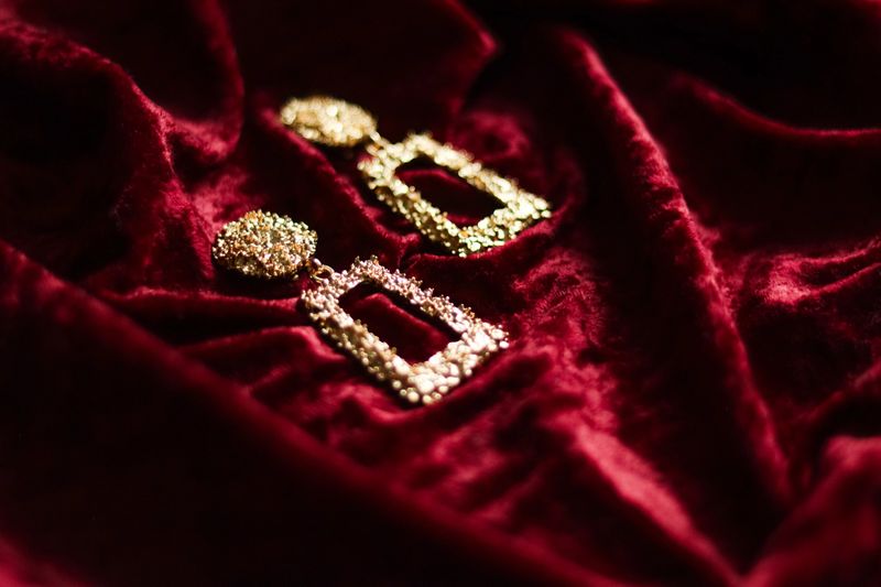 Golden textured statement earrings resting on draped dark red velvet fabric, representing opulence, style, and expensive jewelry