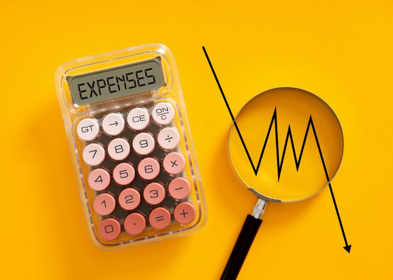 Calculator showing EXPENSES and magnifying glass with a decreasing graph line, symbolizing financial analysis and cost reduction