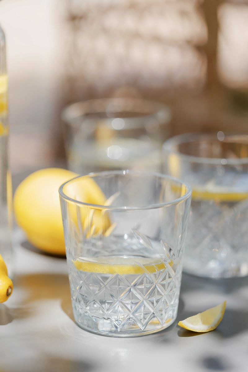 Glassware with lemon slices and fresh lemons arranged on a table in soft dappled light â perfect healthy summer refreshment