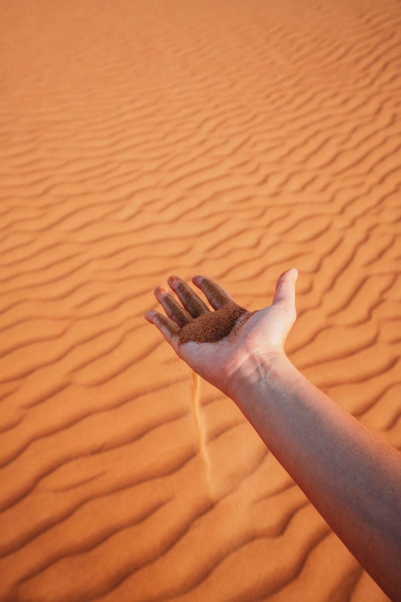 Hand releasing fine desert sand, illustrating concepts of time passing, change, and ephemeral moments in a natural environment