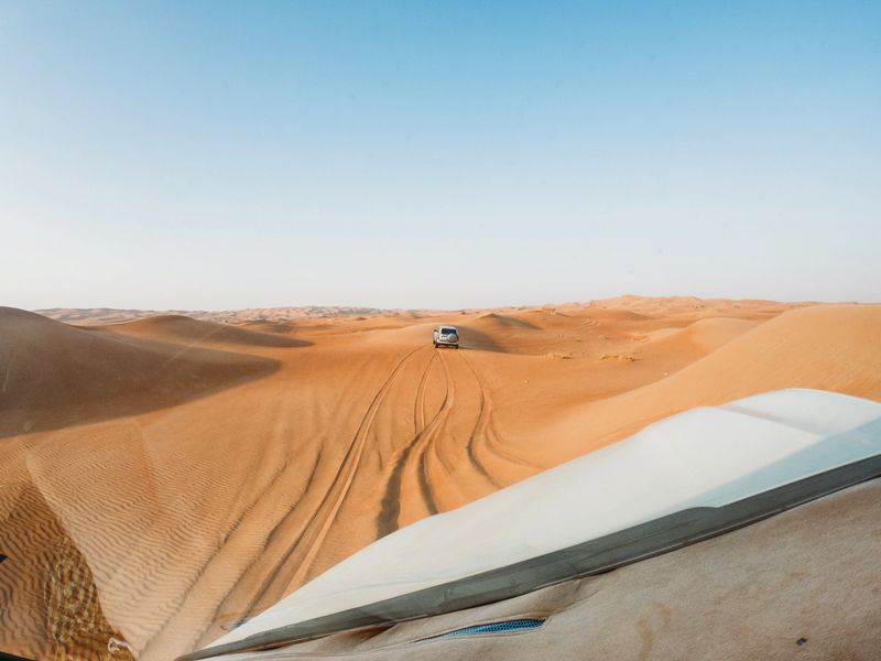 Safari vehicles traversing golden sand dunes under a clear blue sky, experiencing desert adventure in the United Arab Emirates