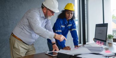 Two engineers reviewing blueprints at a desk.