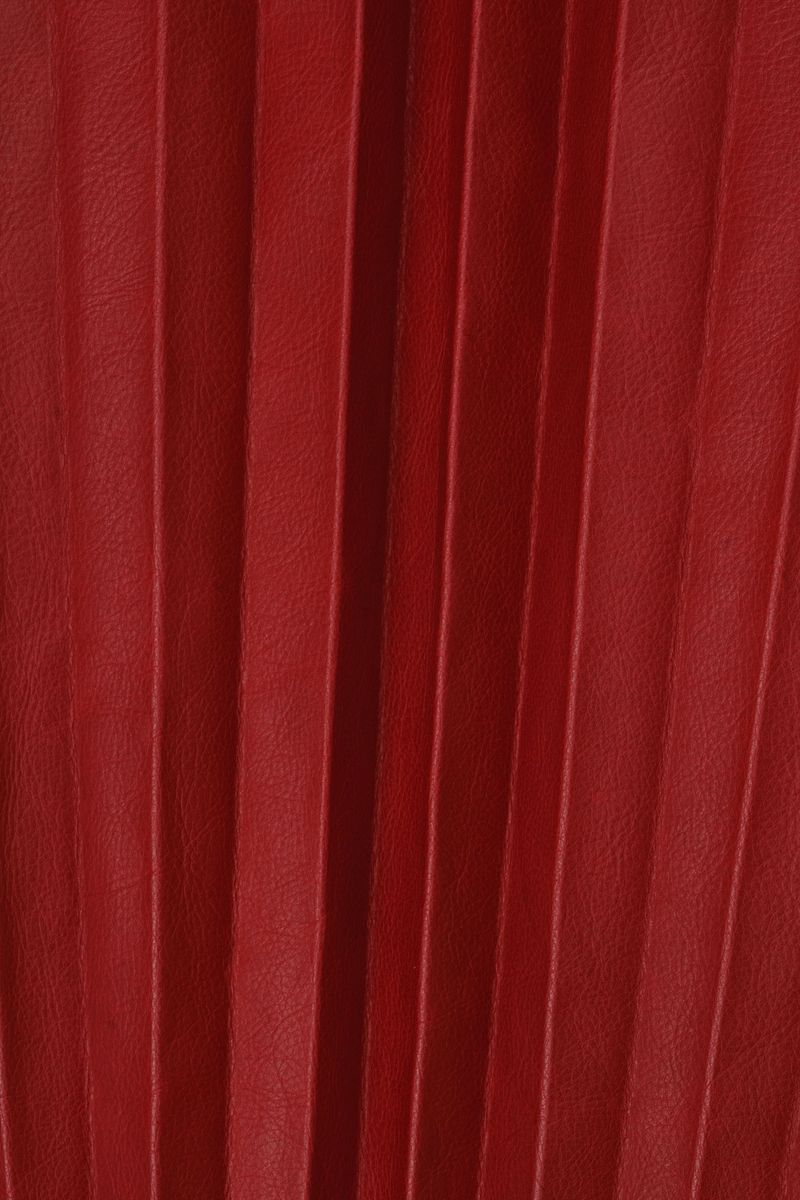 Close-up of pleated genuine red leather texture. Vertical graphic folds, structured surface, rich muted red color, abstract fashion background, no objects
